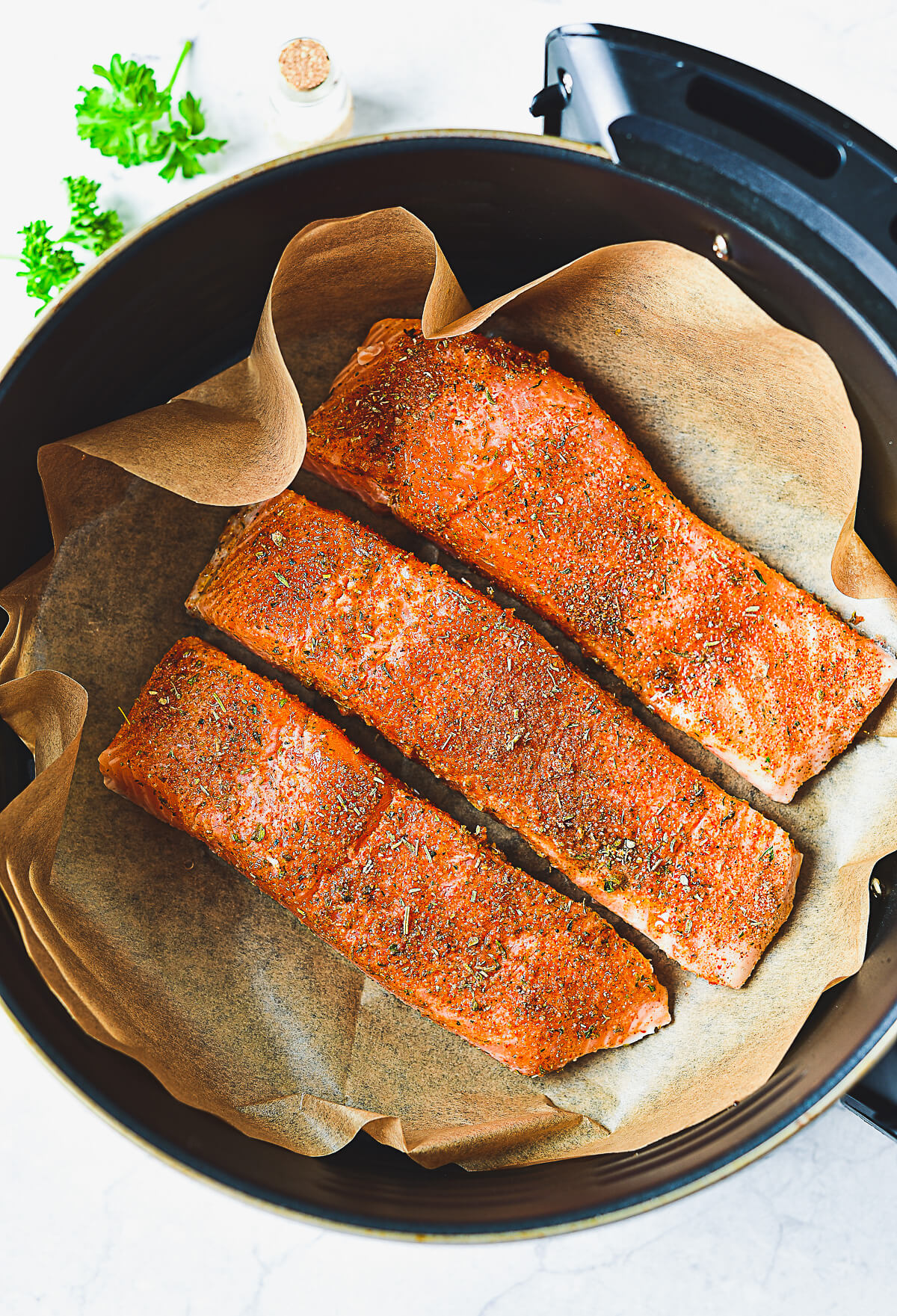 three seasoned salmon fillets in an air fryer basket.