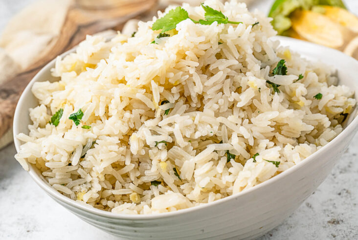 A white bowl full of Ginger Rice accented by bits of garlic, ginger, and fresh cilantro.