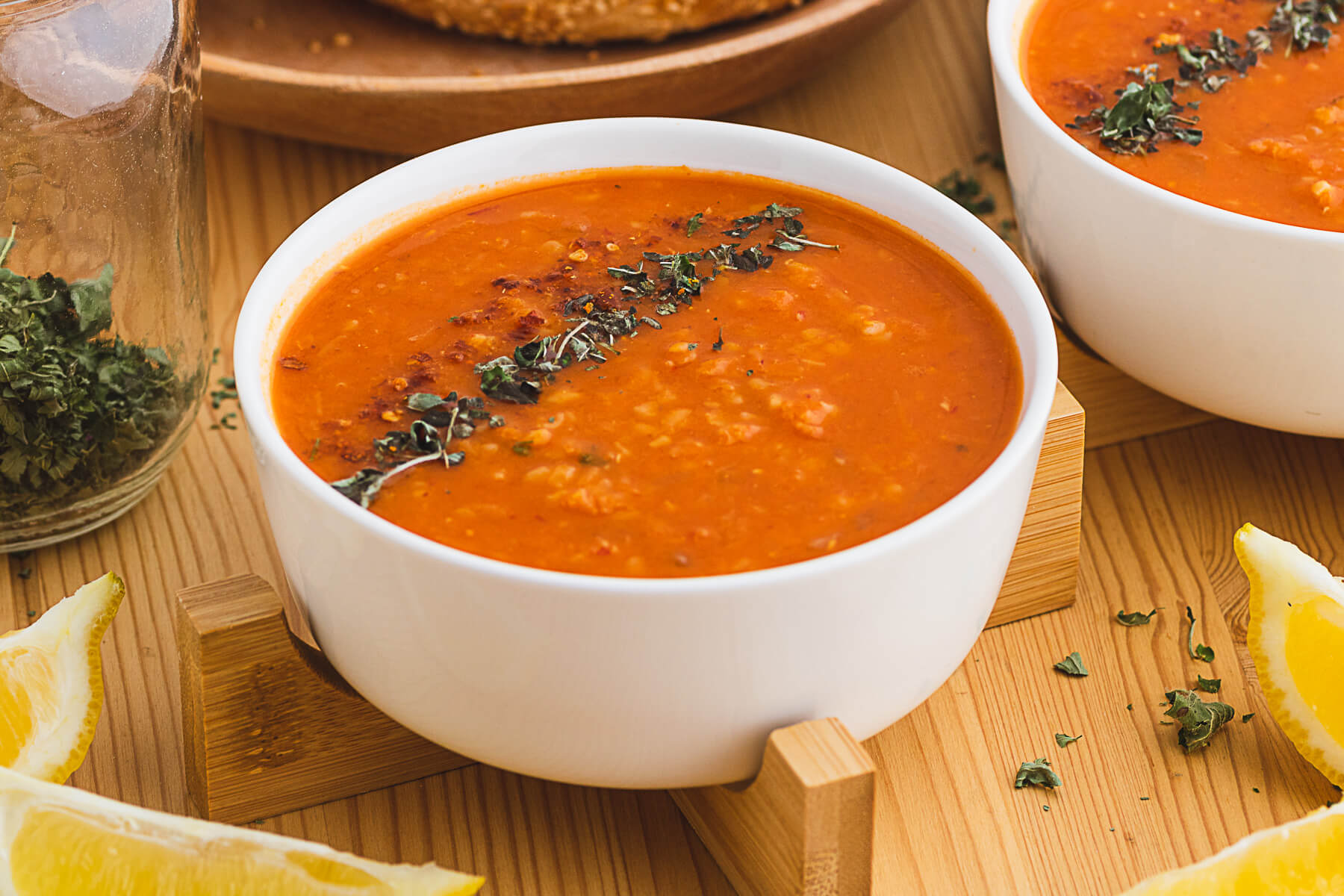 Two white bowls filled with fiery red Turkish Lentil Soup garnished with dried mint and red pepper flakes.