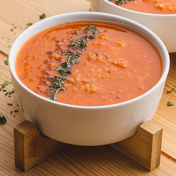 A white bowl filled with fiery red Turkish Lentil Soup garnished with dried mint and red pepper flakes.