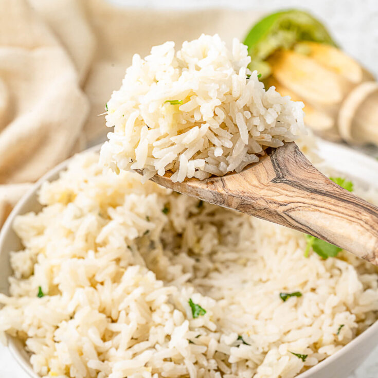 A wooden spoon holds a spoonful of Ginger rice accented with bits of garlic, ginger, and fresh chopped cilantro.