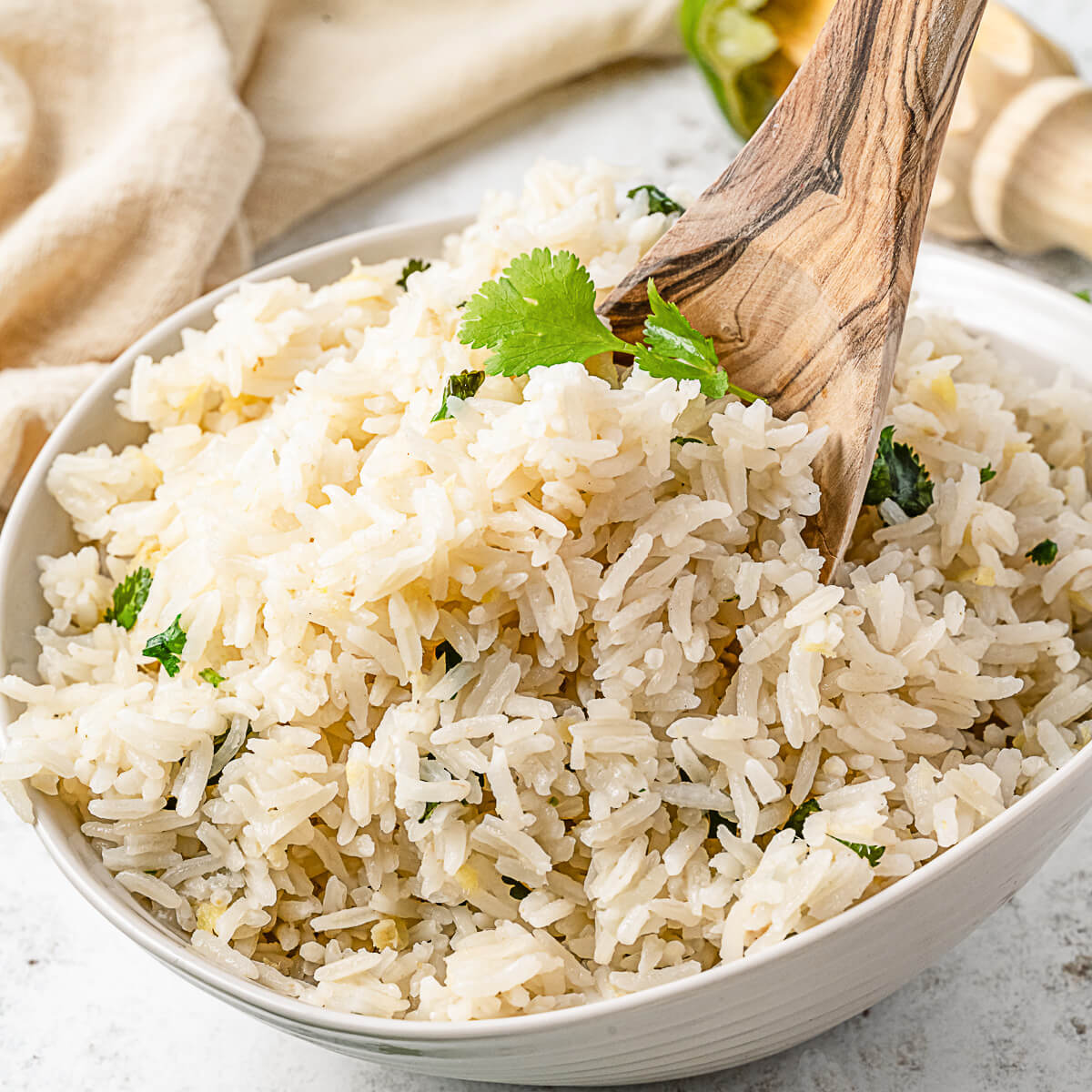 A wooden spoon sits in a white bowl filled with Ginger Rice garnished with chopped cilantro.