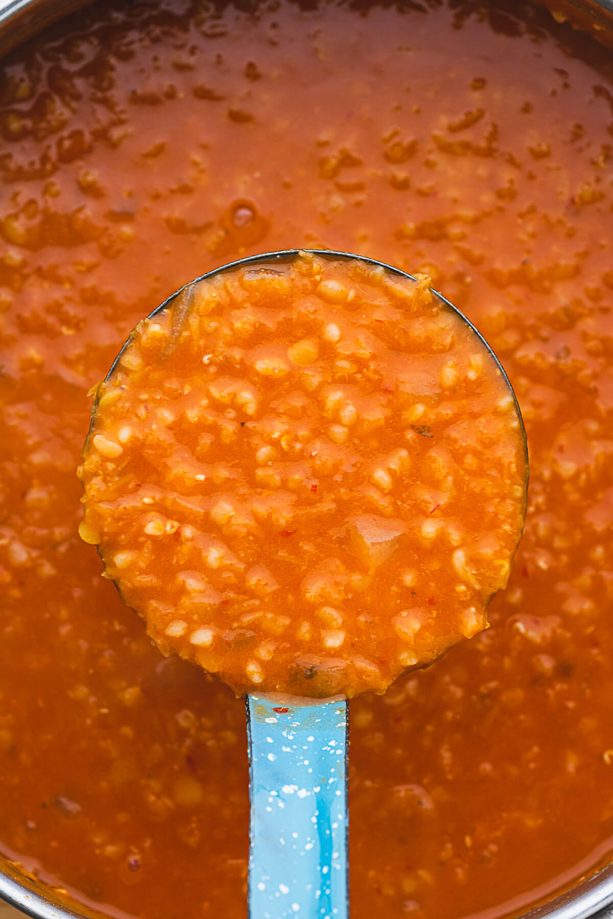Fiery red Turkish lentil soup in a blue enamel ladle. 
