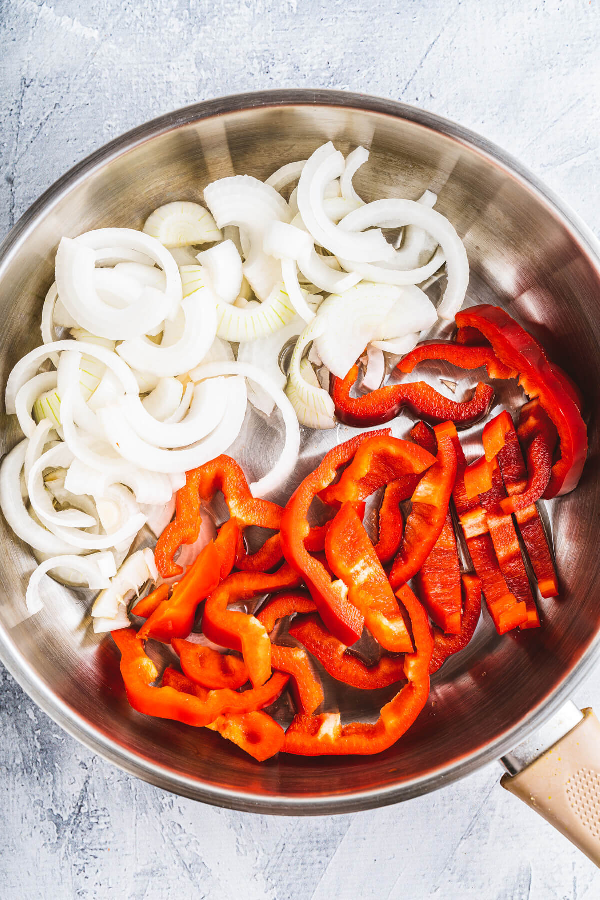 A frying pan containing strips of red bell pepper and sliced white onions.