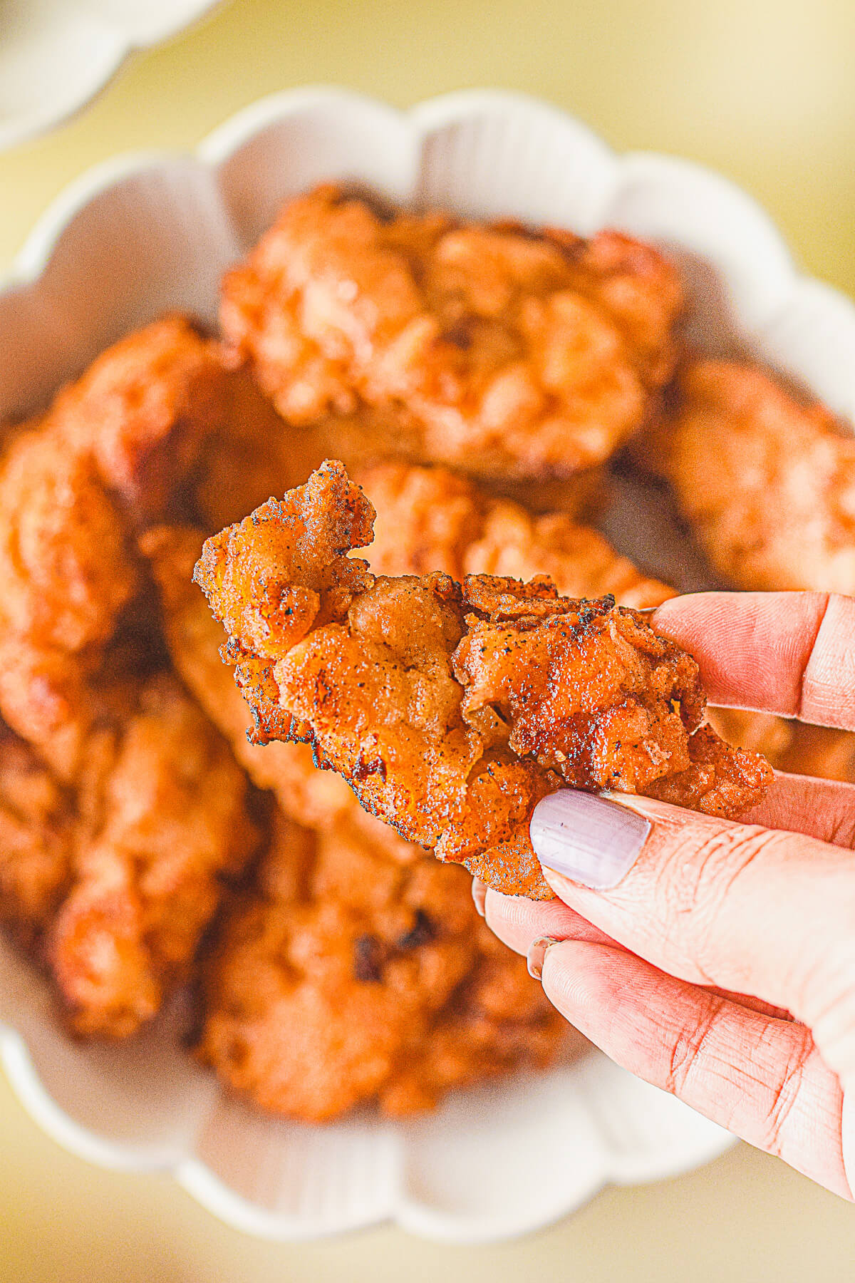 A hand holds a piece of golden fried Mochiko chicken above a dish of fried chicken.