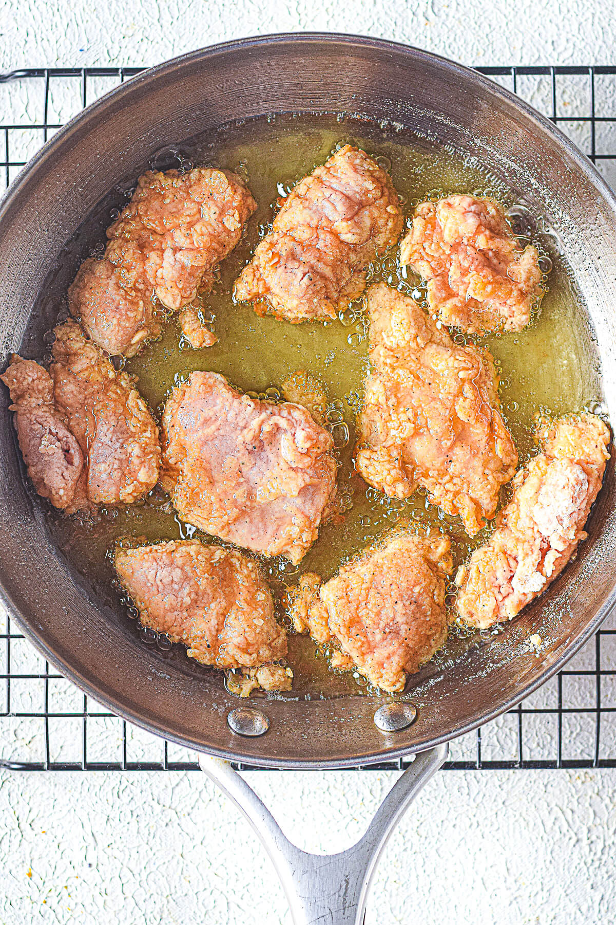 A frying pan filled with oil and frying chicken.