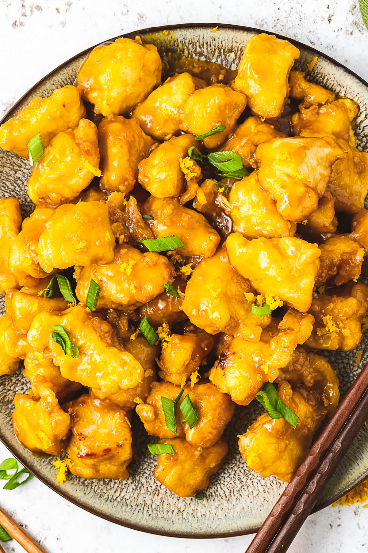 Close up image of Orange chicken garnished with green onions and orange zest.