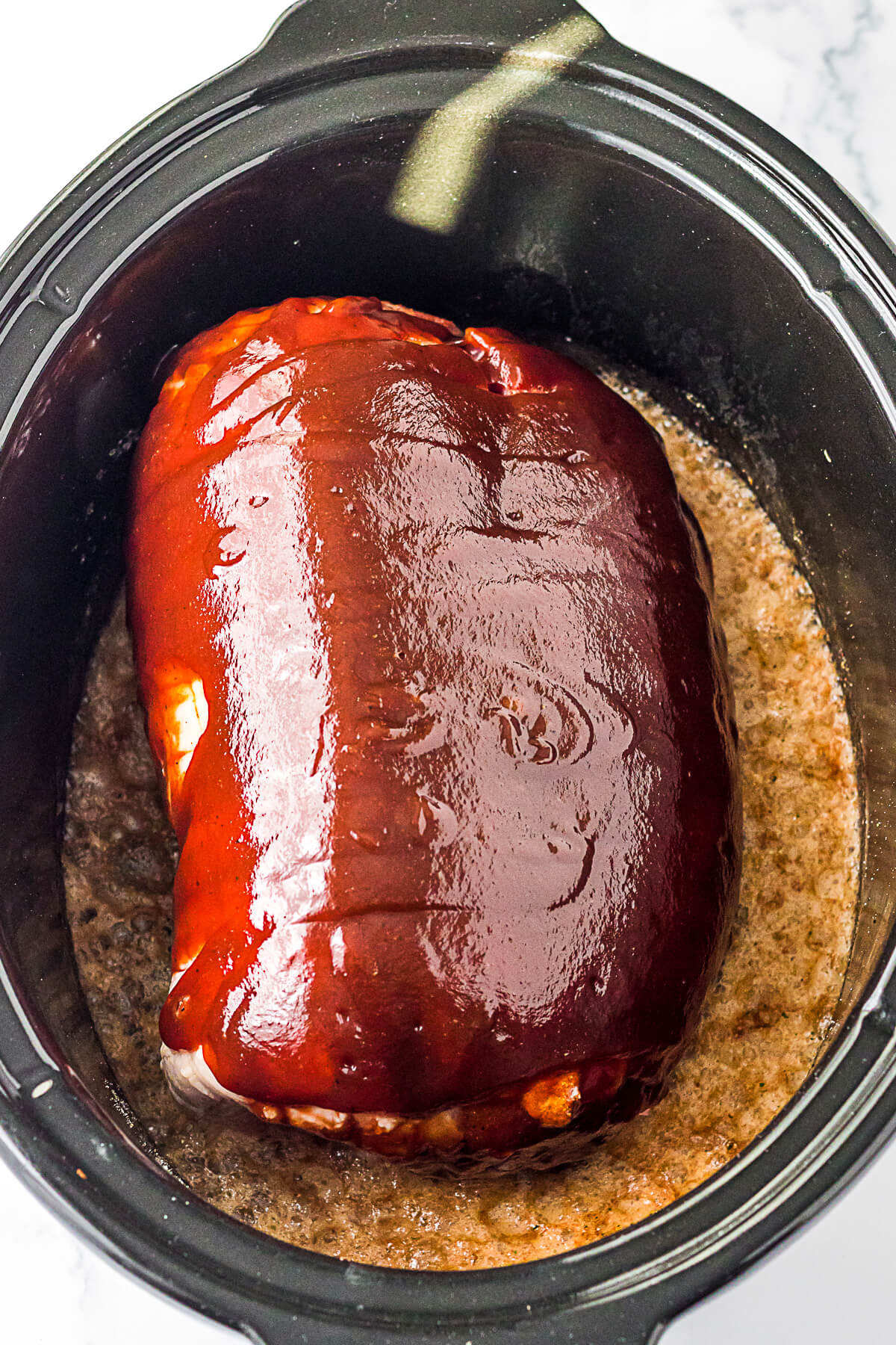 A pork shoulder butt roast covered in barbecue sauce in a slow cooker.