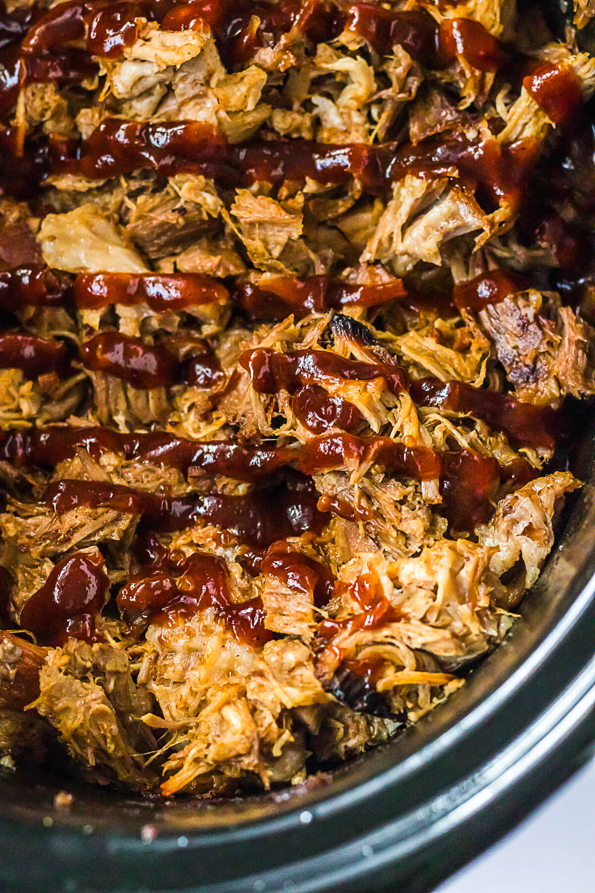 A slow cooker filled with Root beer pulled pork drizzled with barbecue sauce.
