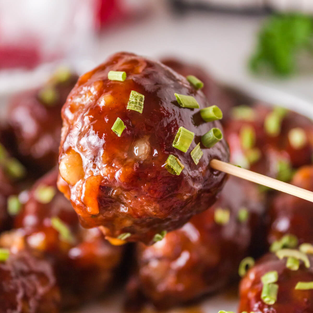 A smoked meatball garnished with chopped green chives on a toothpick.