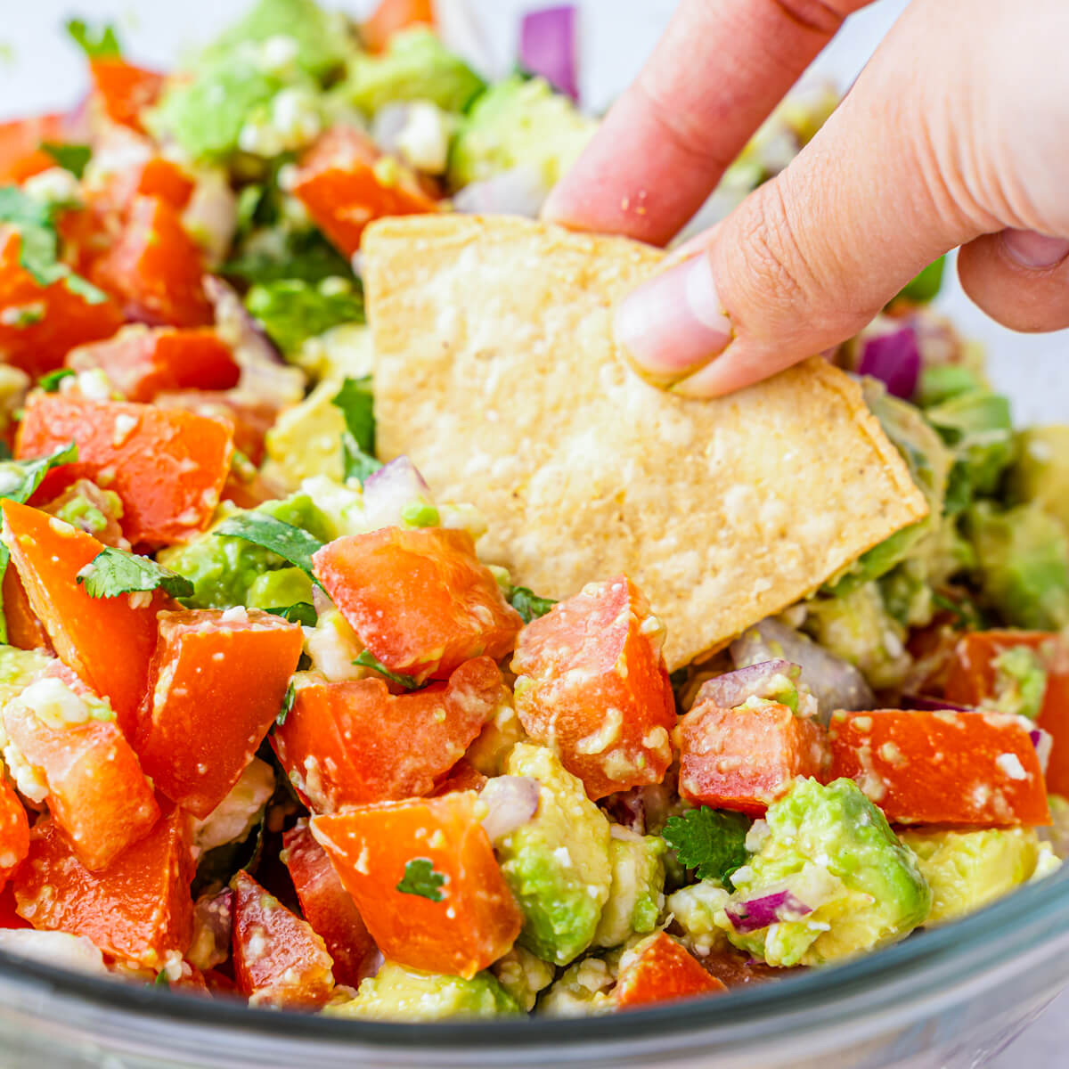 A bowl of chunky avocado salsa with a tortilla chip being dipped into it.