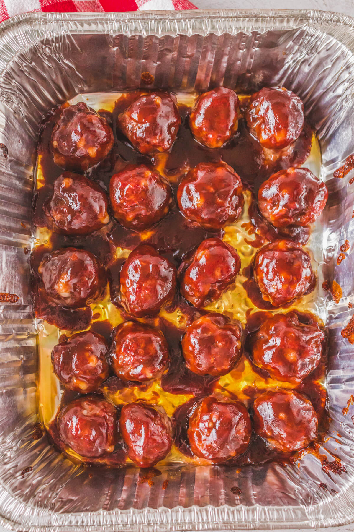 A aluminum tray of smoked meatballs glazed with BBQ sauce.