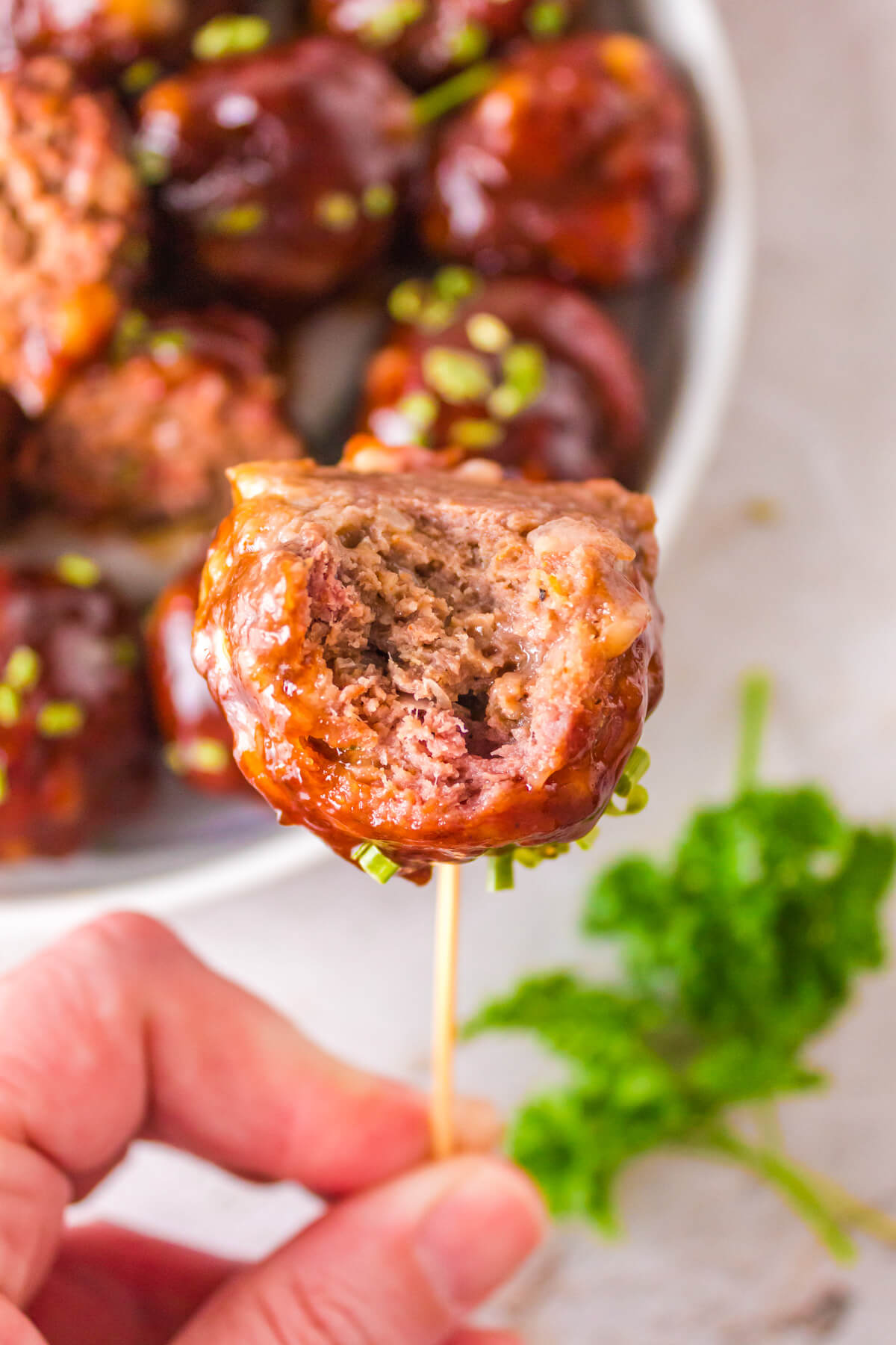 The inside of a smoked meatball garnished with chopped green chives on a toothpick.