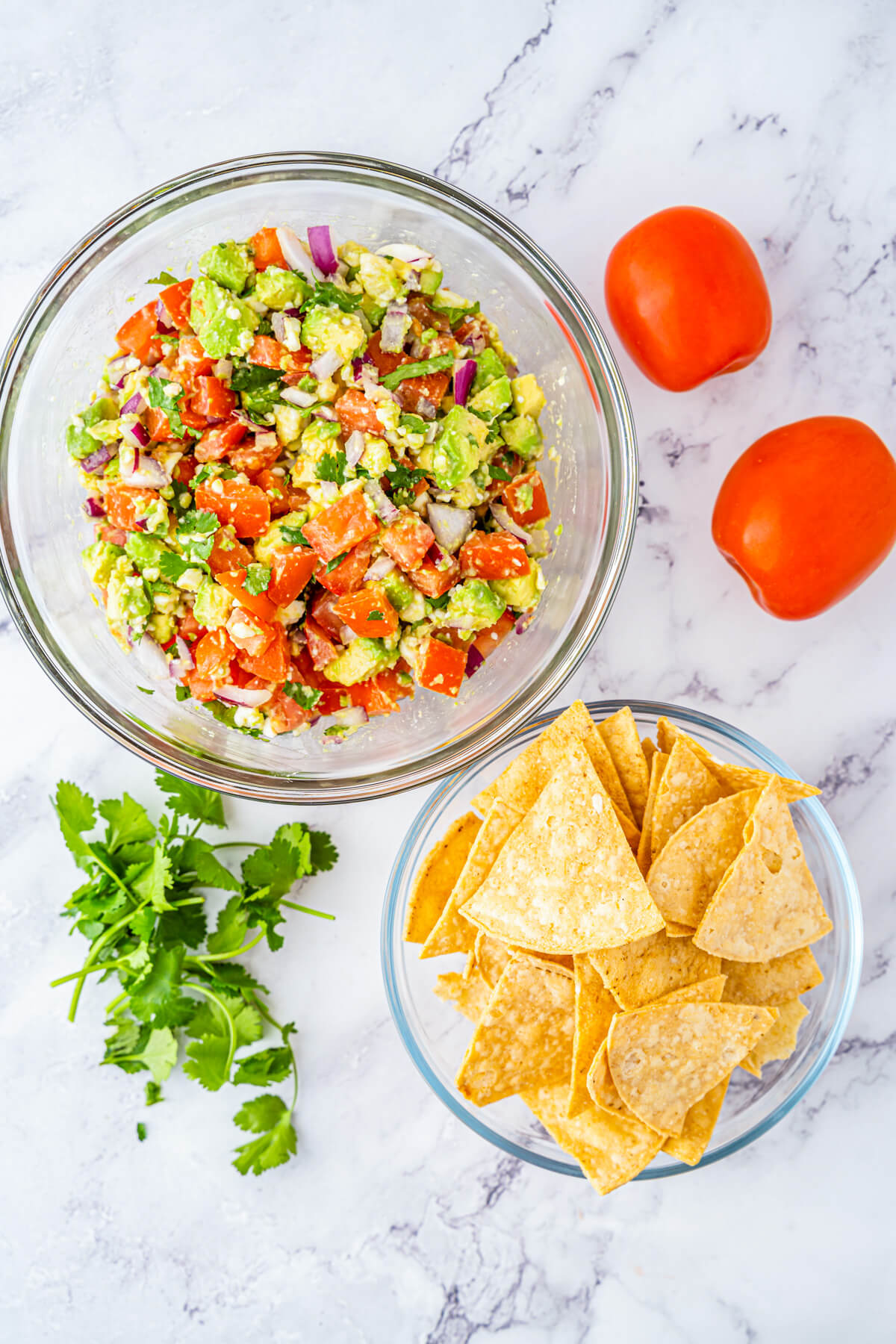 A glass bowl full of chunky avocado salsa featuring avocado, tomatoes, cilantro, Cotija cheese, and red onions.