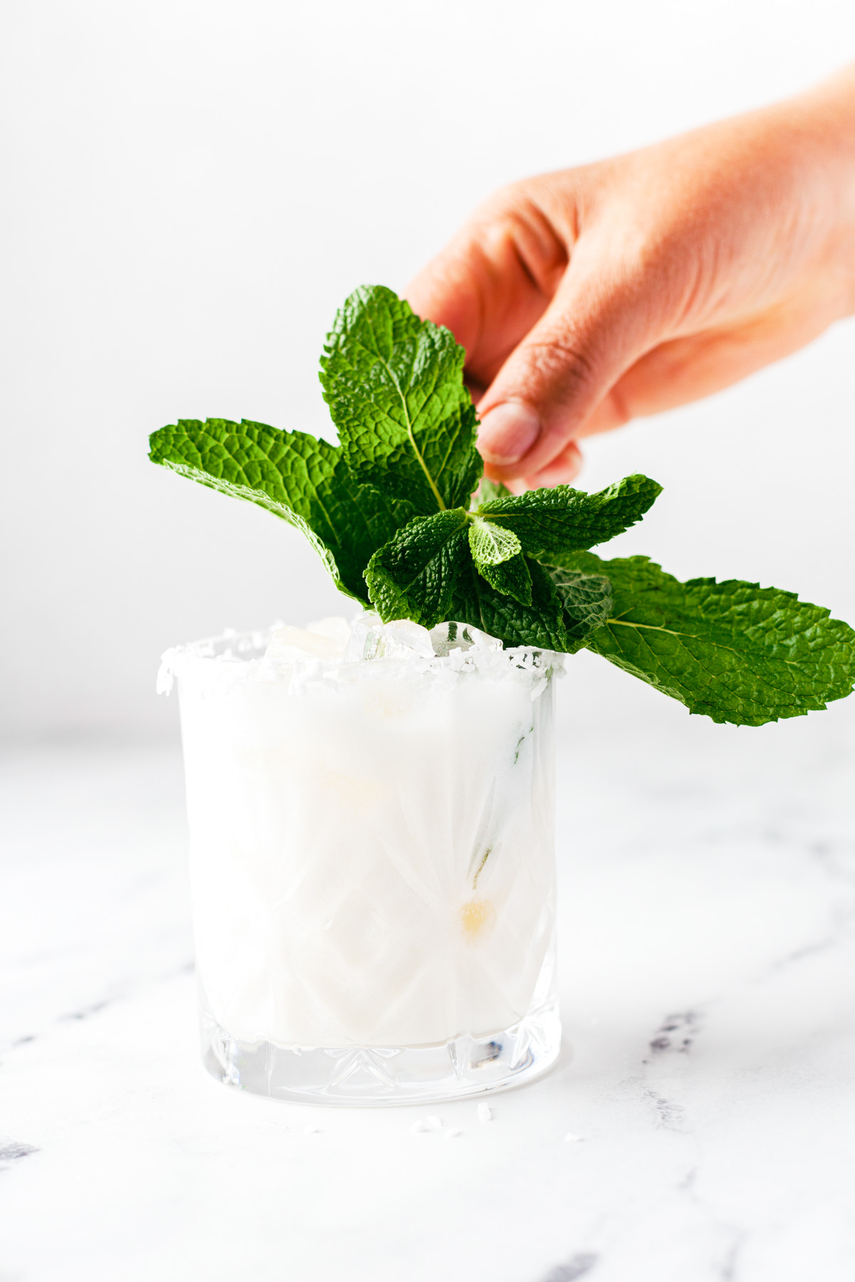 A creamy coconut margarita in a rocks glass rimmed with coconut and garnished with fresh mint.