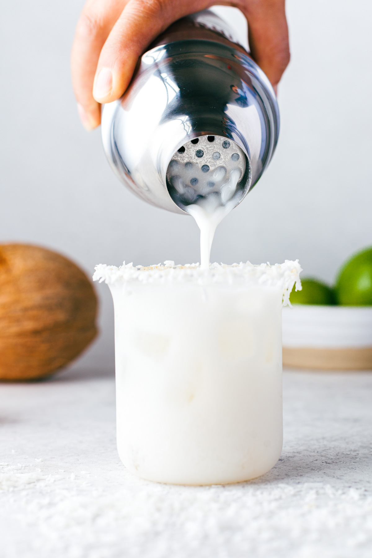 A shaken Coconut Margarita being poured into a coconut rimmed rocks glass.