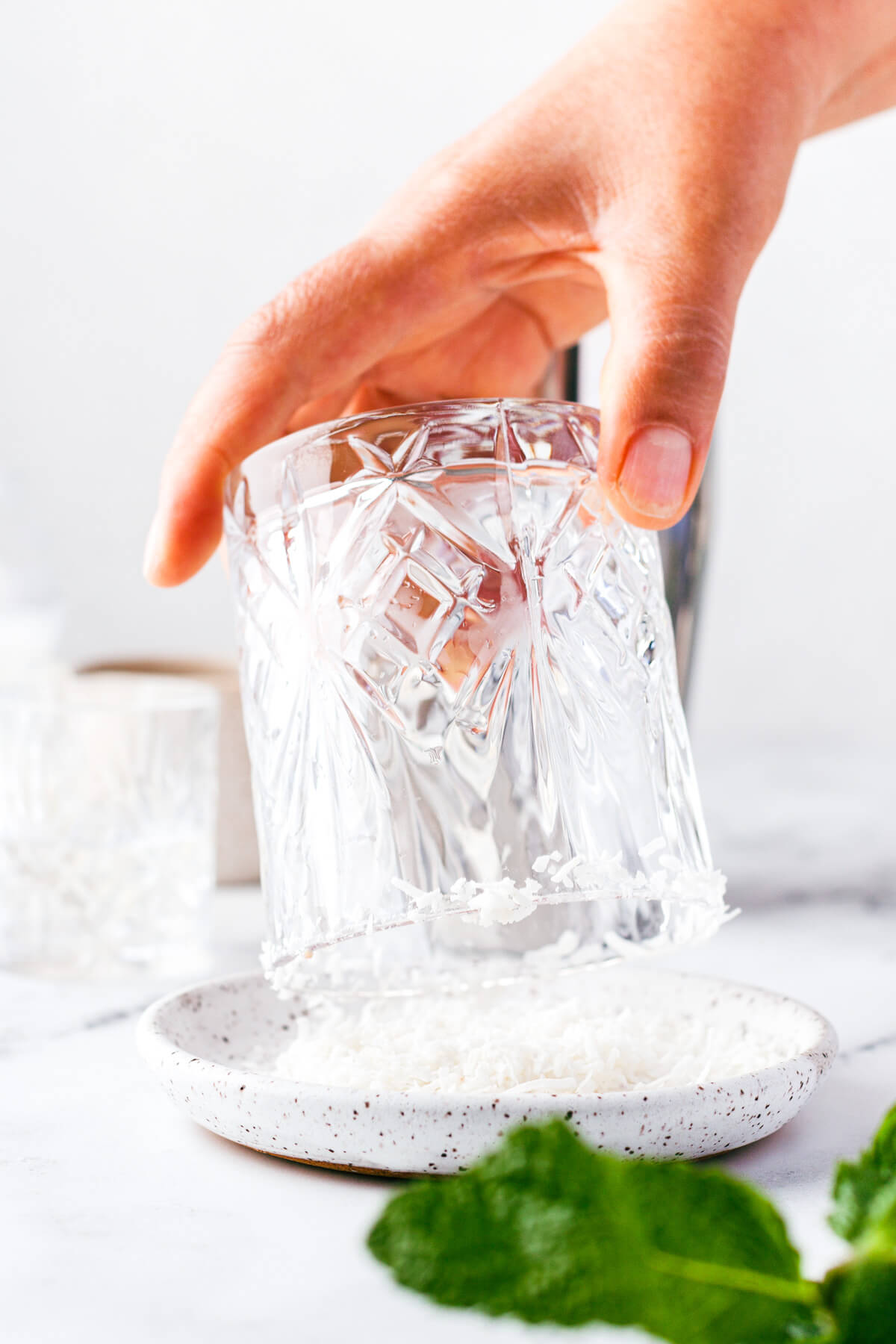 Rimming a rocks glass with sugar and shredded coconut.