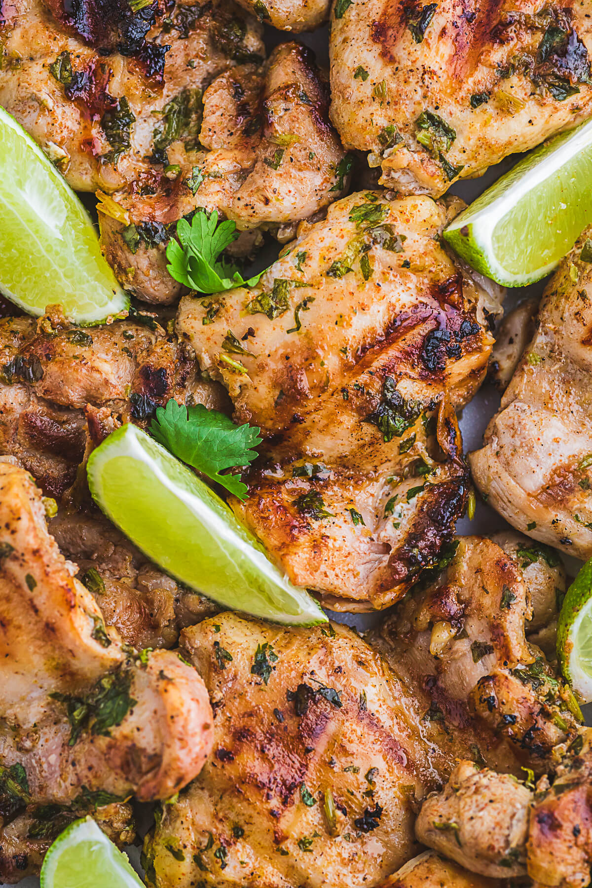 A platter of grilled chicken thighs topped with chopped fresh cilantro and lime wedges.