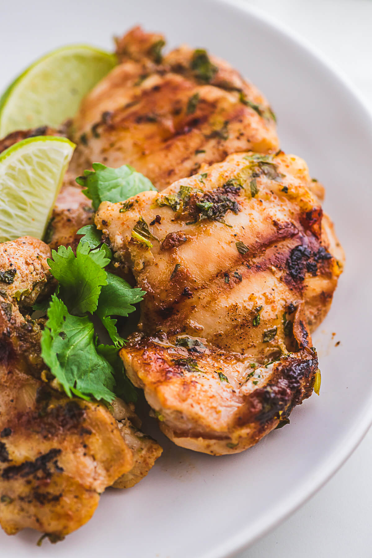 A plate of grilled chicken thighs garnished with cilantro and served with lime wedges.