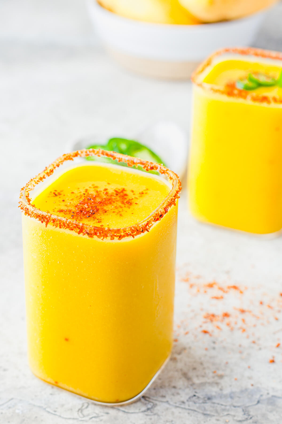 Two square rocks glasses filled with with vibrant spicy mango margarita garnished with Tajin seasoning.