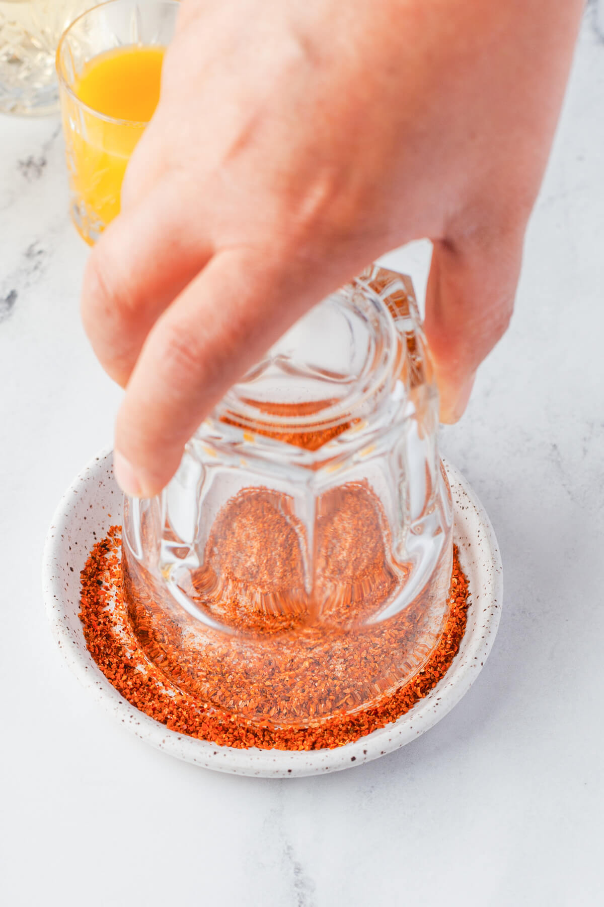 A cocktail glass being dipped in a salt and Tajin seasoning rimmer.