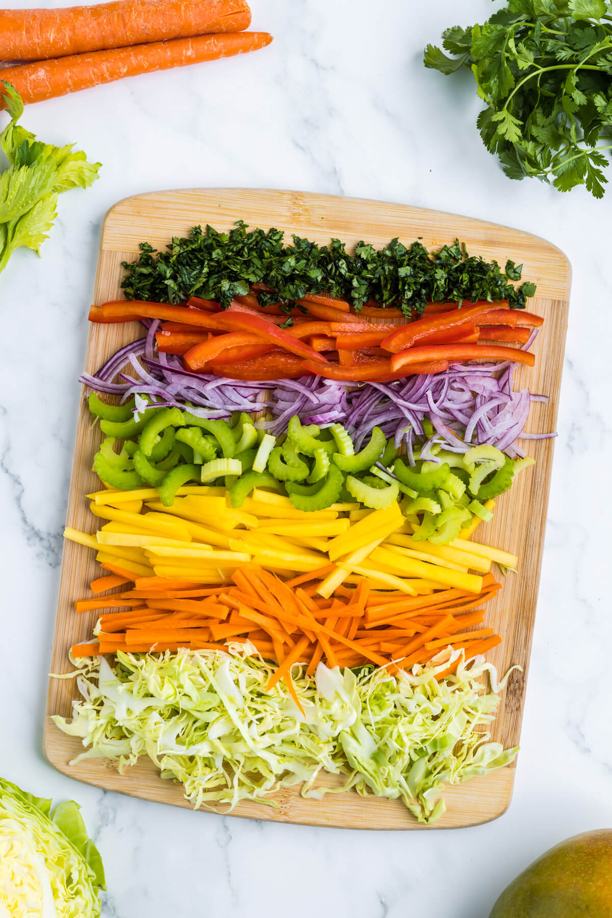A rainbow of sliced coleslaw vegetables and mango on a cutting board.