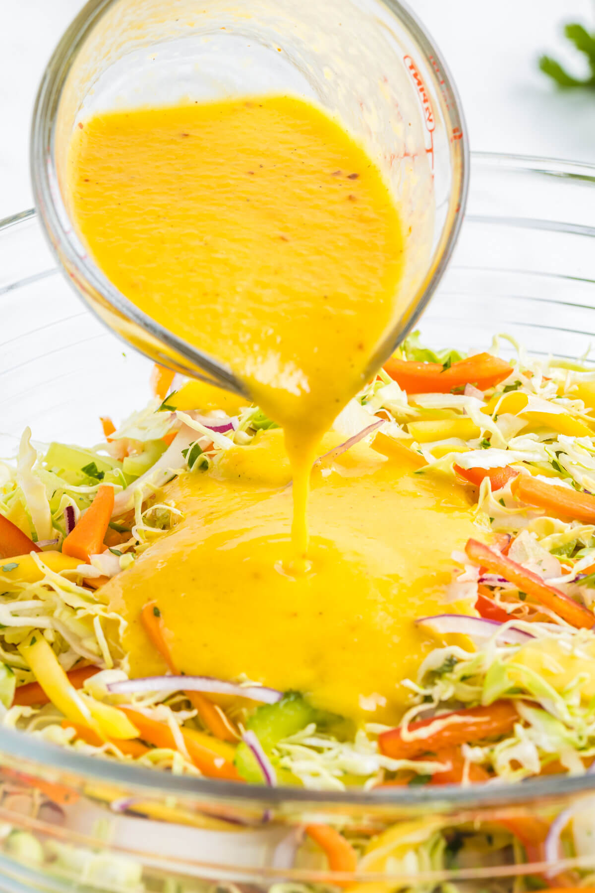 Mango salad dressing being poured over a bowl of shredded coleslaw mix.