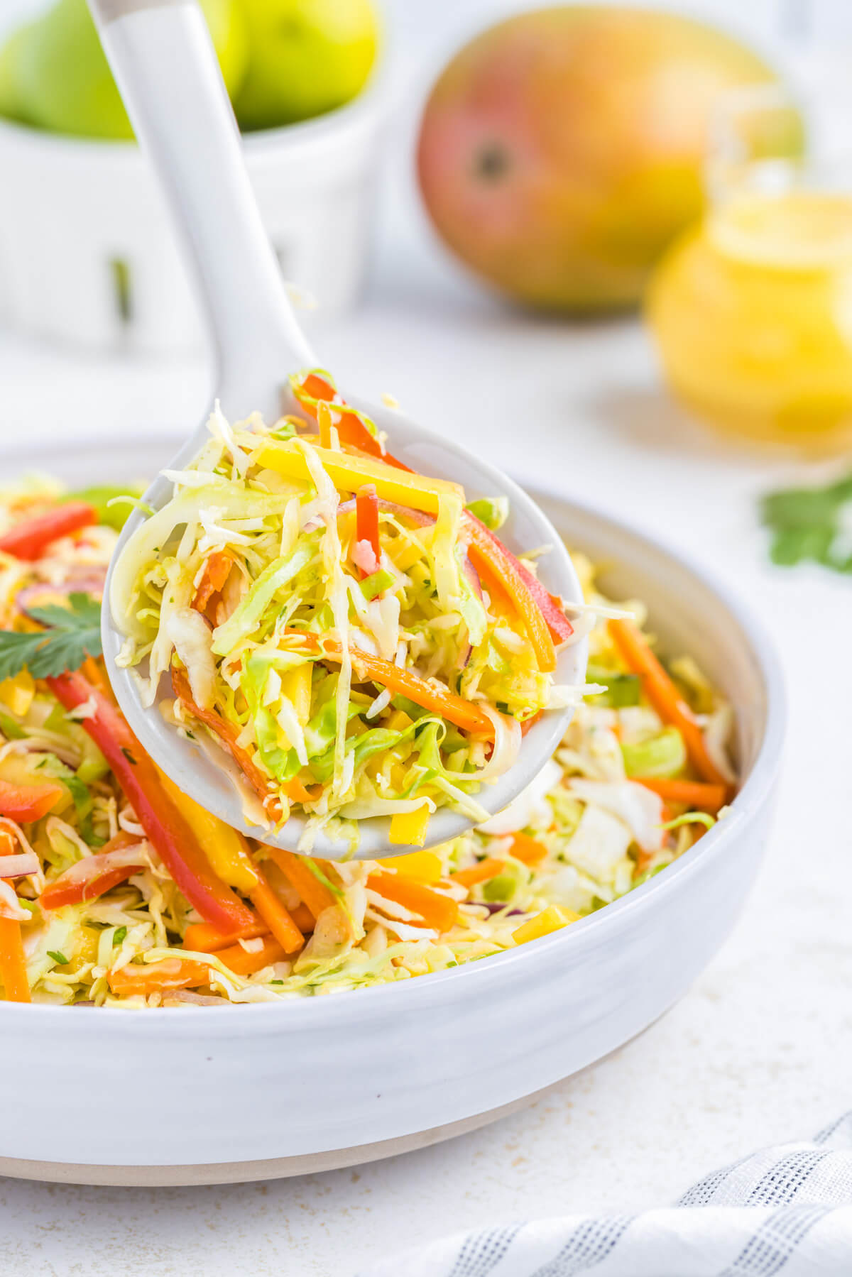 A white spoon holds a scoop of colourful mango slaw.