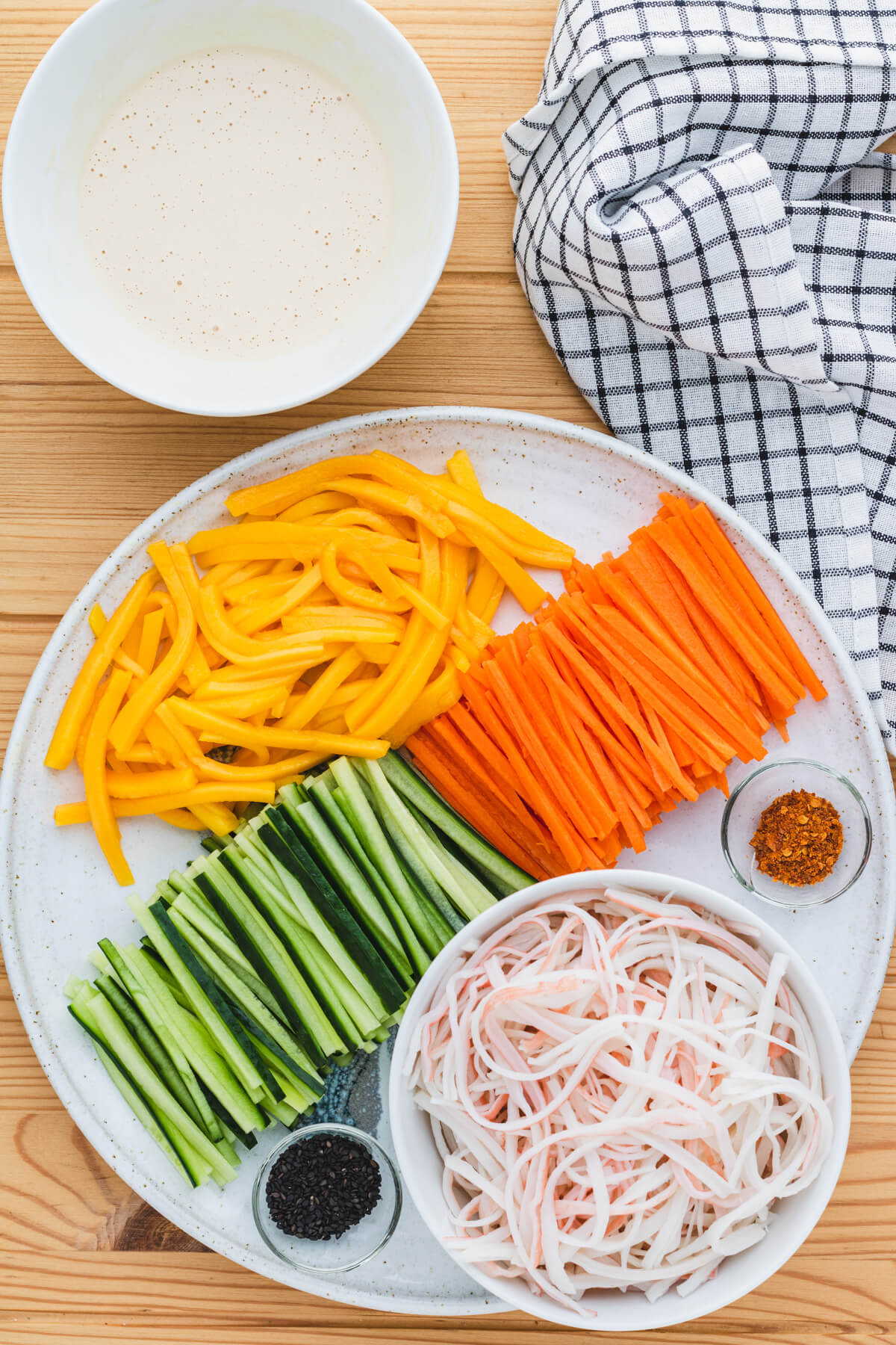 Chopped ingredients for Kani Salad arranged on a platter beside a bowl of Kewpie mayonnaise dressing.