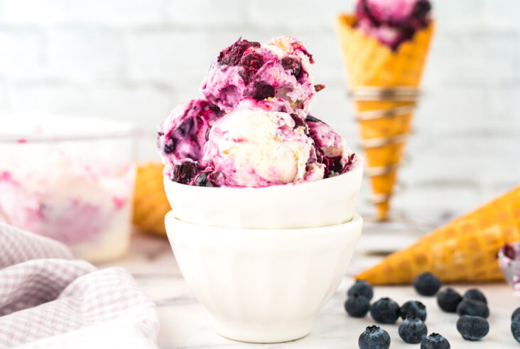 A stack of white bowls filled with creamy Blueberry Cheesecake Ice Cream.