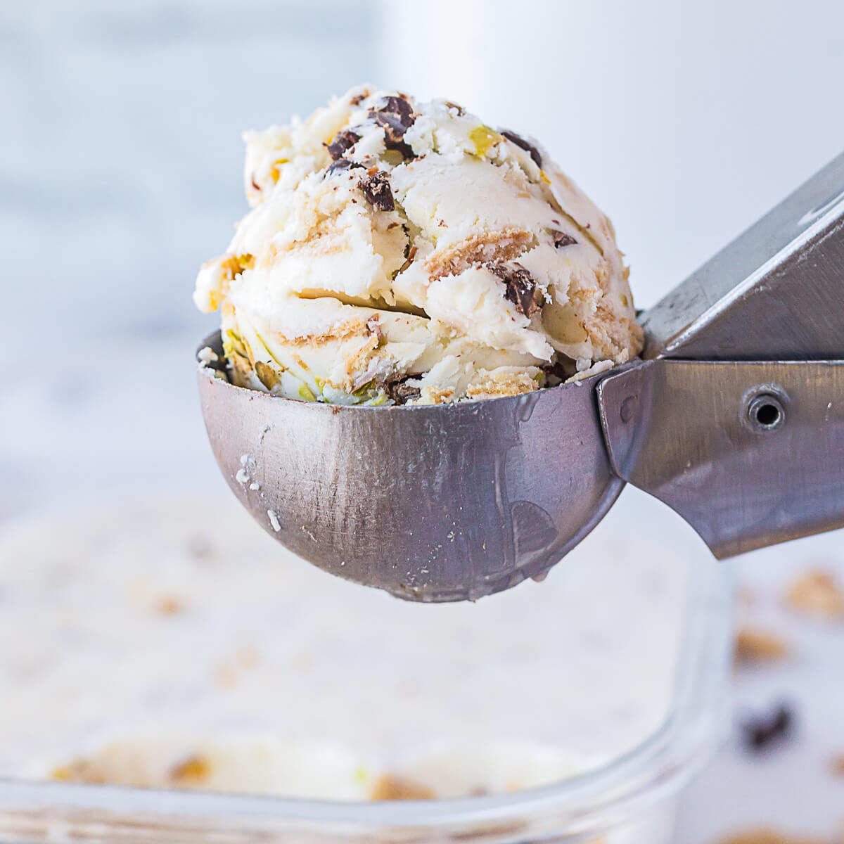 An ice cream scoop full of white vanilla ice cream dotted with chocolate chips, pistachios, and broken sugar cone bits.