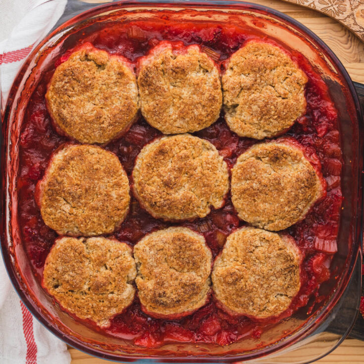 A glass baking dish filled with vibrant red strawberry rhubarb cobbler.