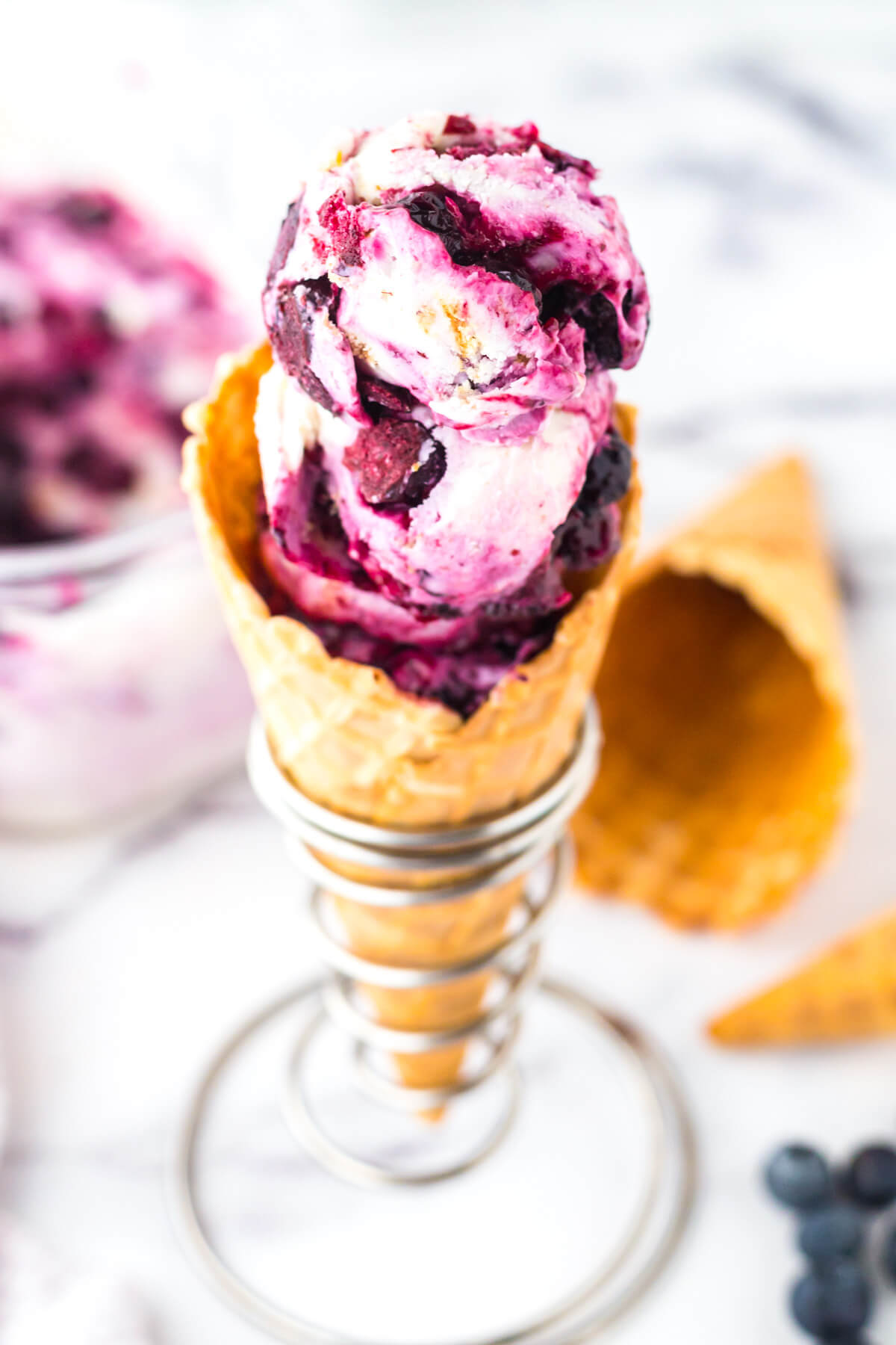 An ice cream cone holding a scoop of vibrant purple Blueberry Cheesecake Ice Cream.