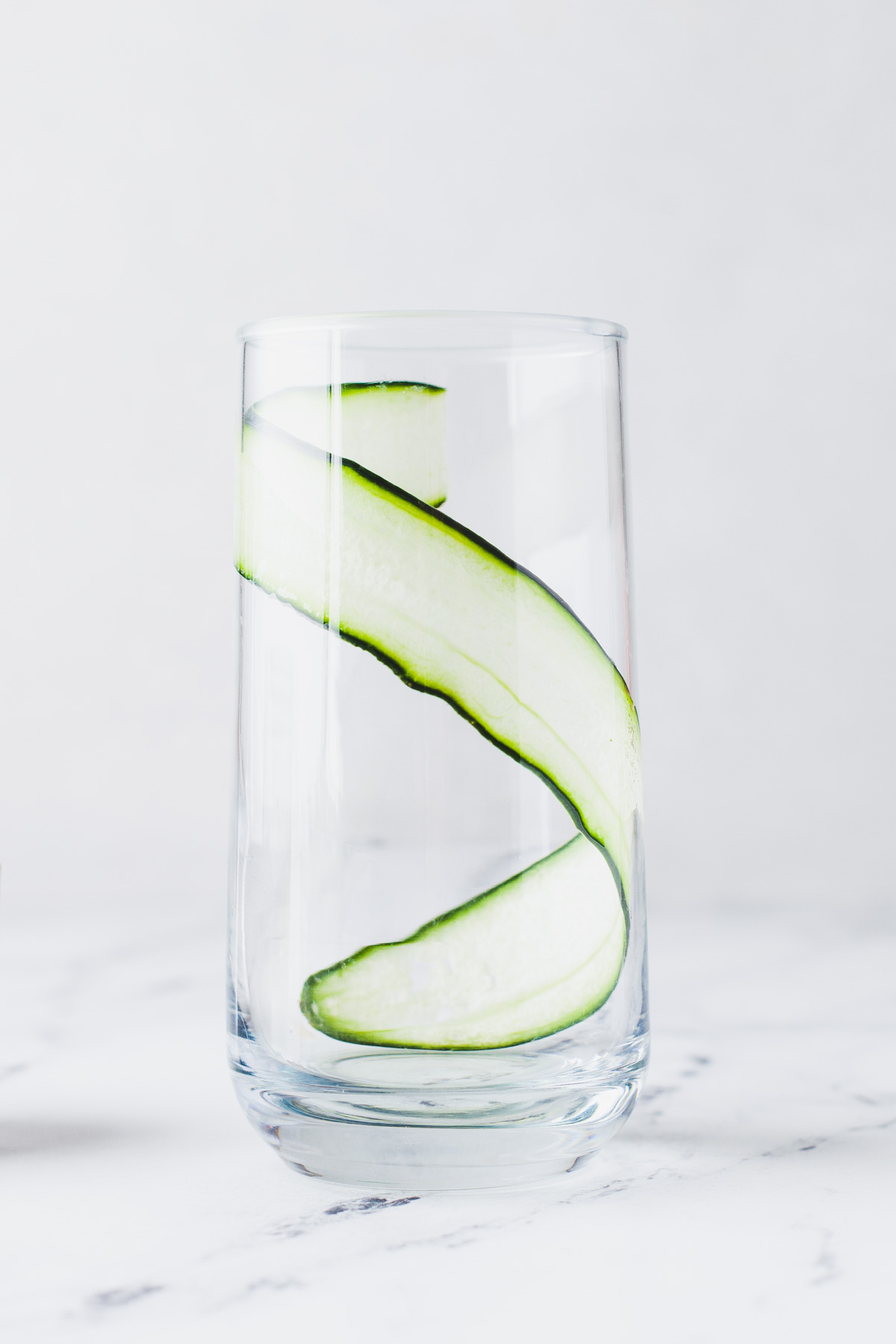 An empty cocktail glass showing how to stick a long thin slice of cucumber onto the side of the glass. 