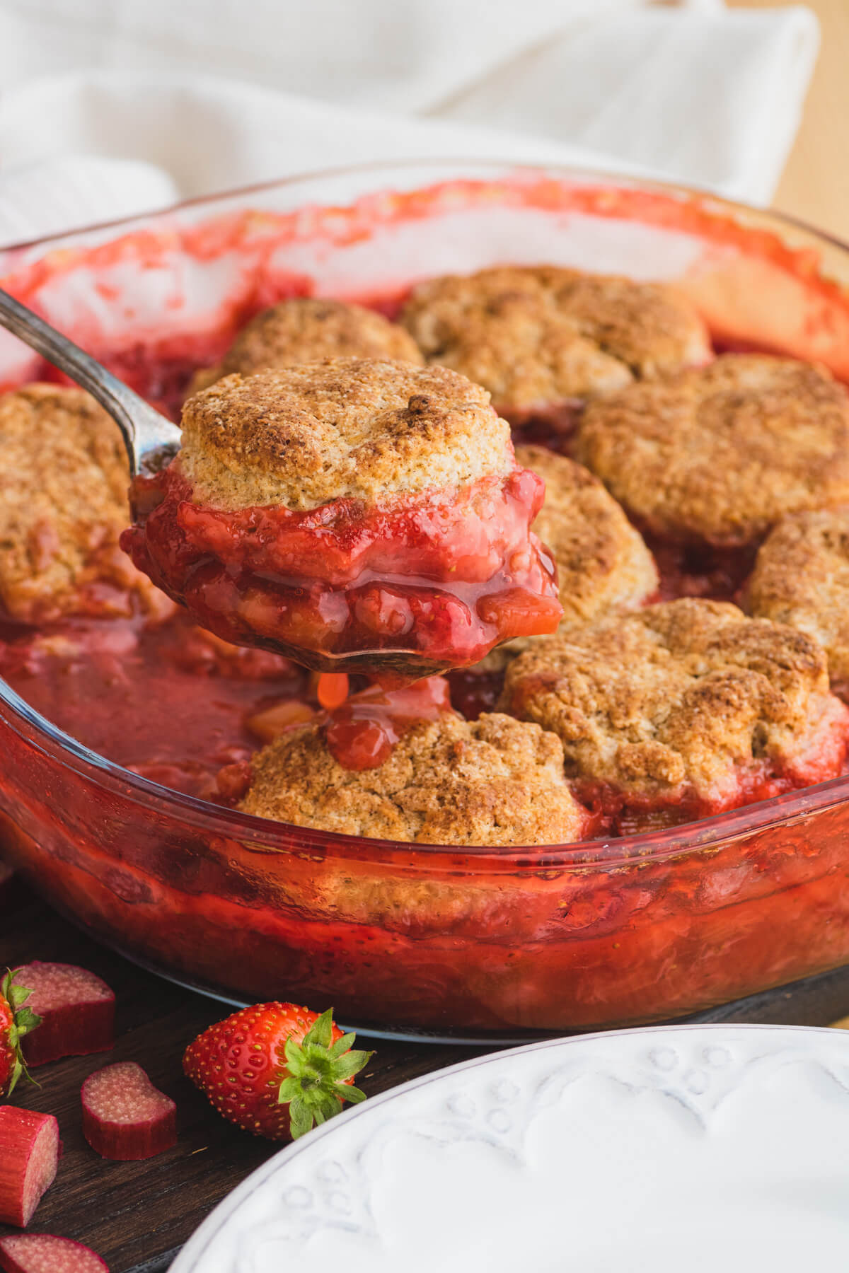 A silver vintage serving spoon serves up a portion of strawberry rhubarb cobbler.