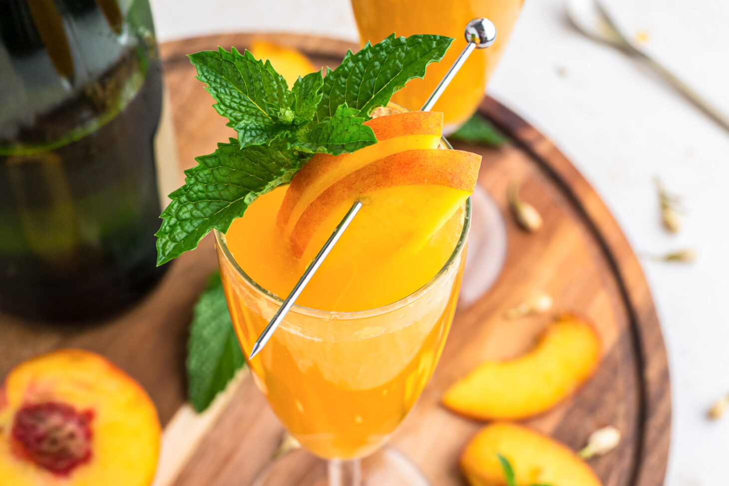 One peach bellini cocktail in a champagne glass garnished with a spring of fresh mint and sliced peaches.