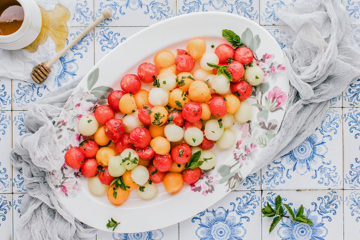 Melon salad featuring colourful melon balls arranged on an oval platter with scattered fresh mint leaves.