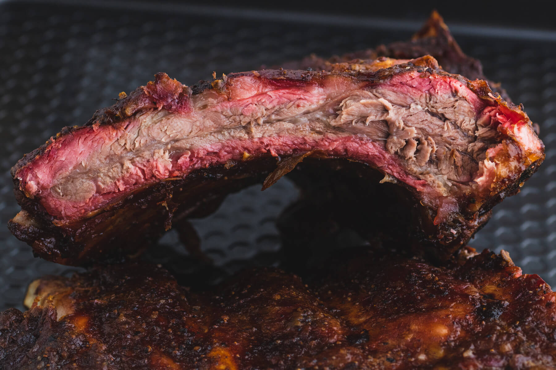 A side view of a smoked beef back rib showing the vibrant smoke ring.