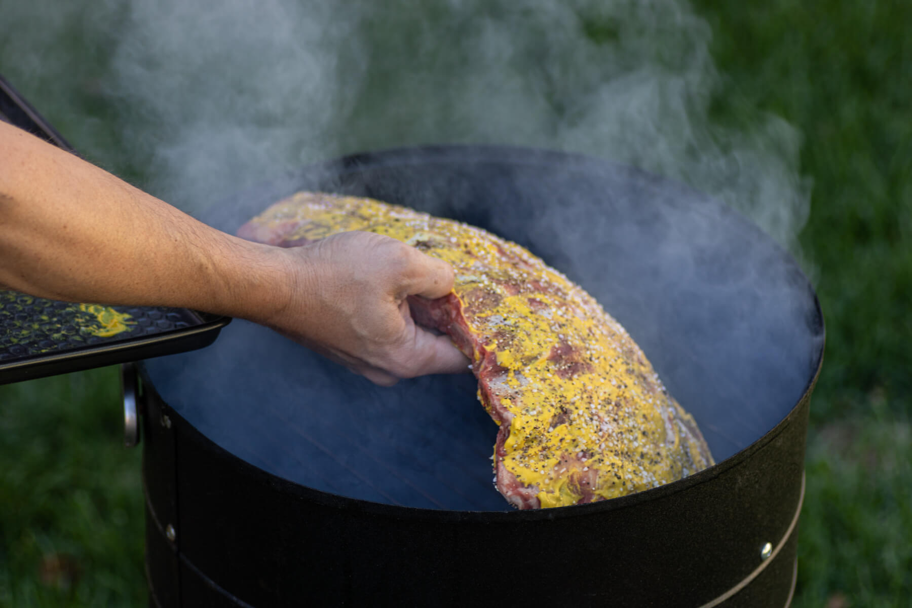 A hand places mustard coated ribs into a smoker.