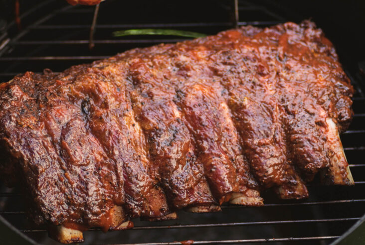 A rack of saucy smoked beef ribs on a grill.