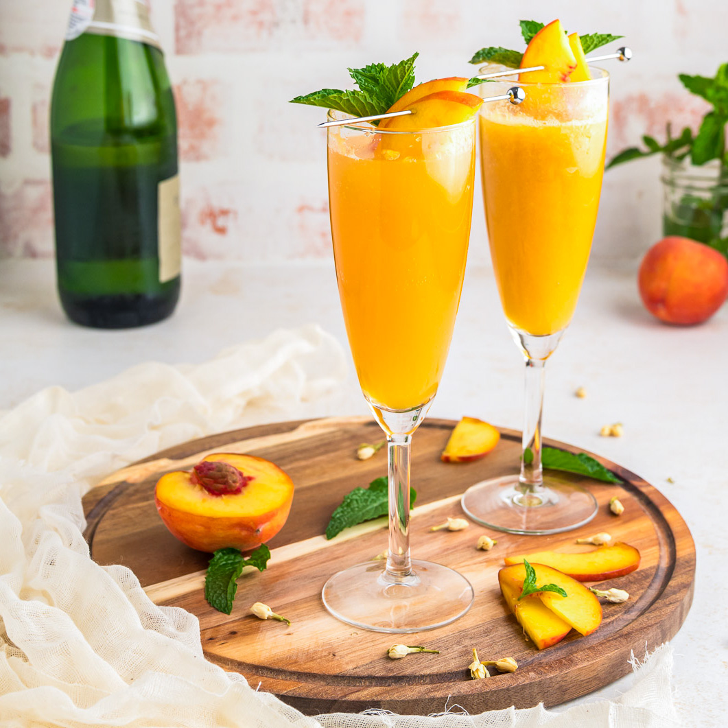 Two champagne glasses on a wooden tray filled with Peach Bellini cocktail.