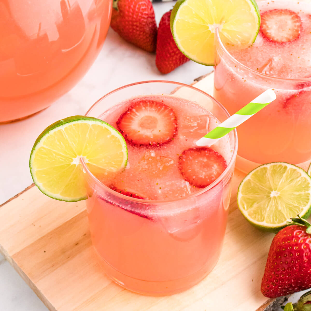 A glass full of pink Strawberry Limeade garnished with sliced strawberries and lime wheels.