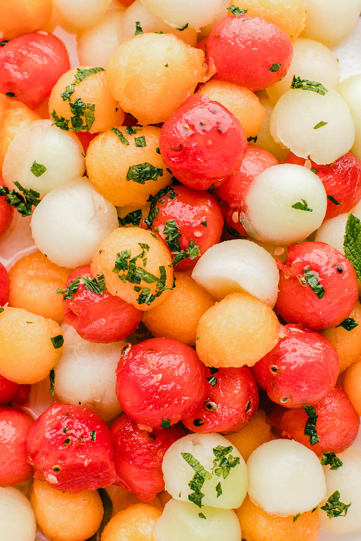 Close up of multicoloured melon balls scattered with fresh mint leaves.