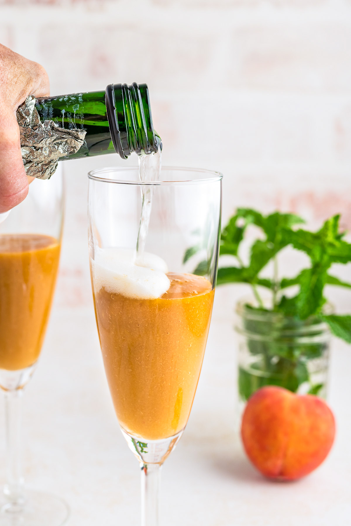 A hand pours prosecco into a champagne glass filled with peach puree.