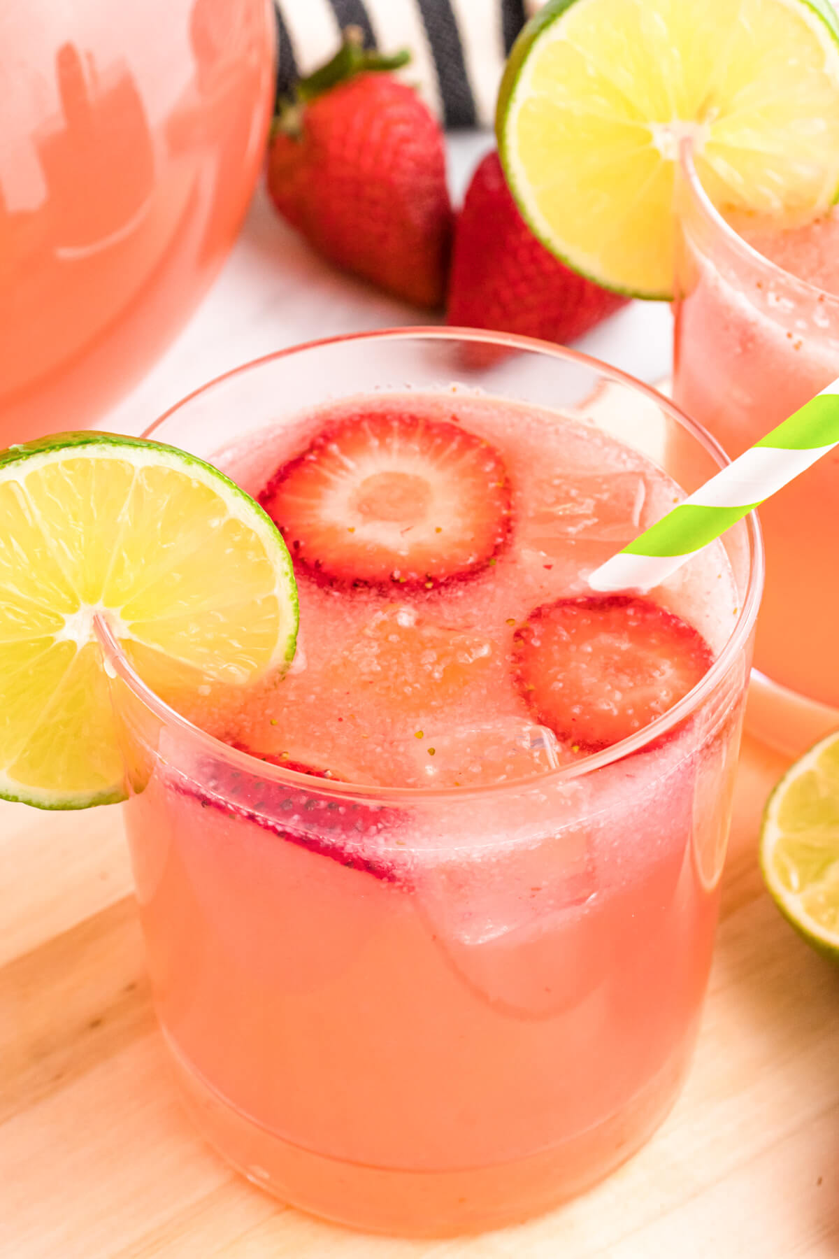 A glass pitcher and glass full of pink Strawberry Limeade garnished with sliced strawberries and lime wheels.