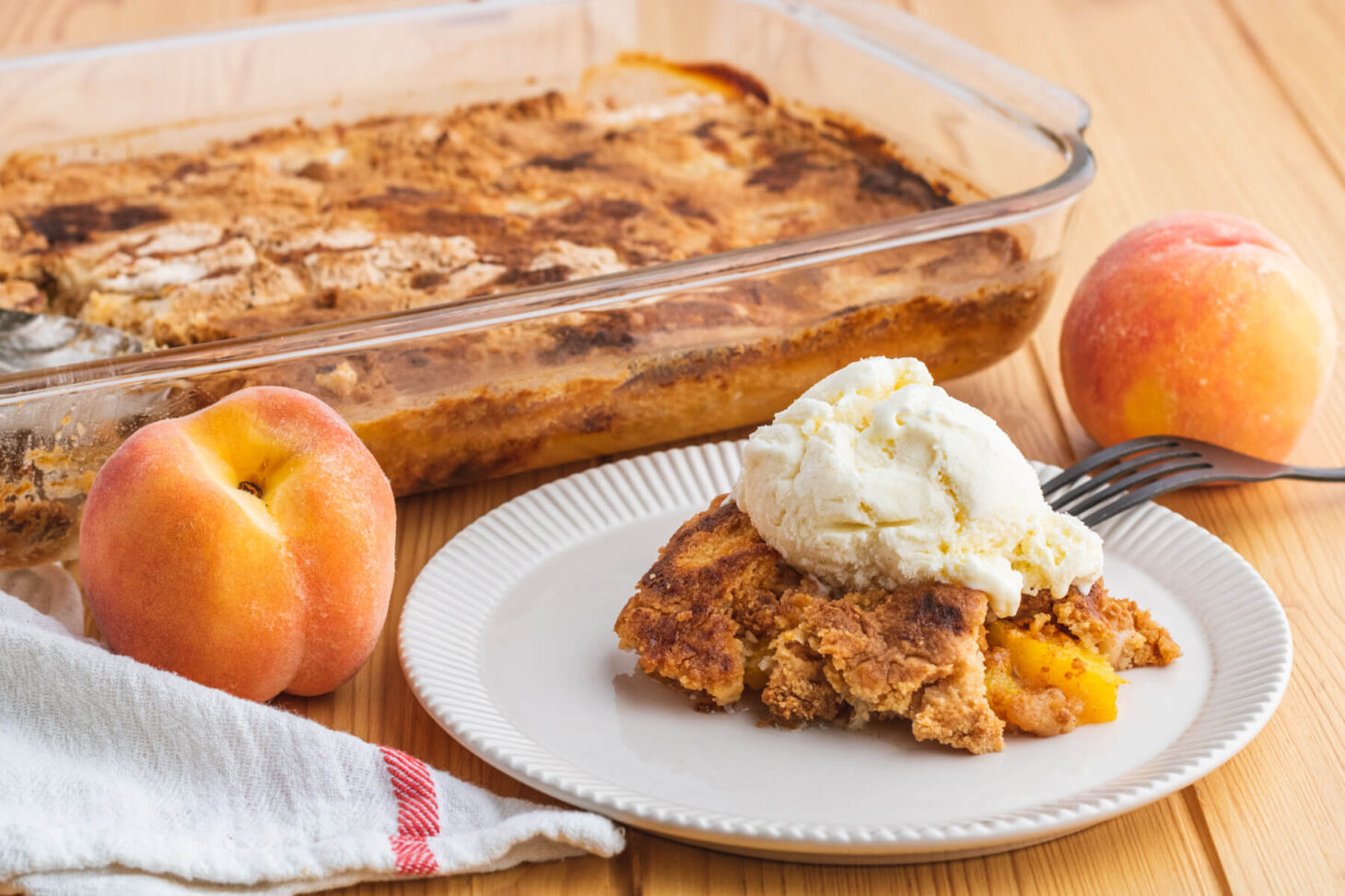 A white plate containing a scoop of peach cobbler dump cake topped with a scoop of ice cream.