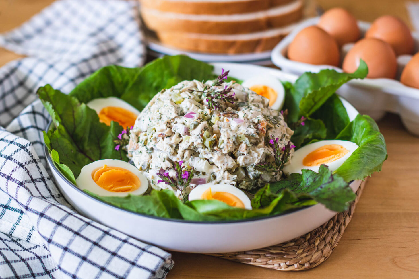 A lettuce lined bowl containing a scoop of Chicken egg salad and hard boiled egg halves with bright yellow yolks.