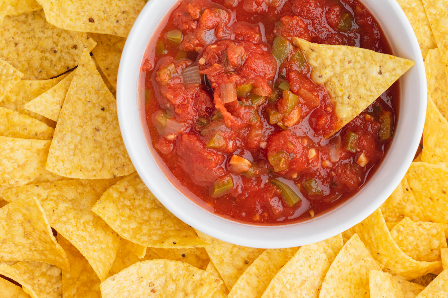 A white bowl filled with chunky canned salsa surrounded by tortilla chips.