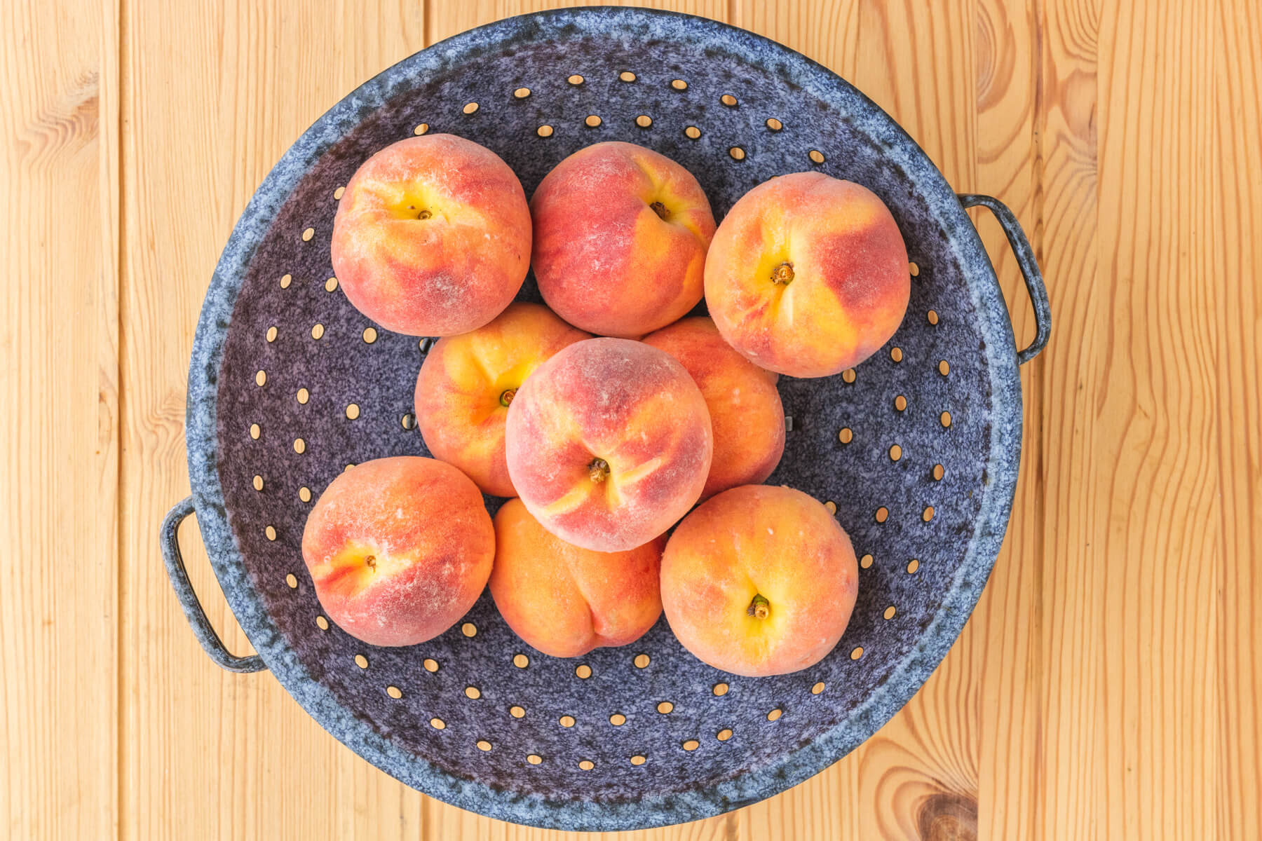 An enamel colander containing fresh peaches.