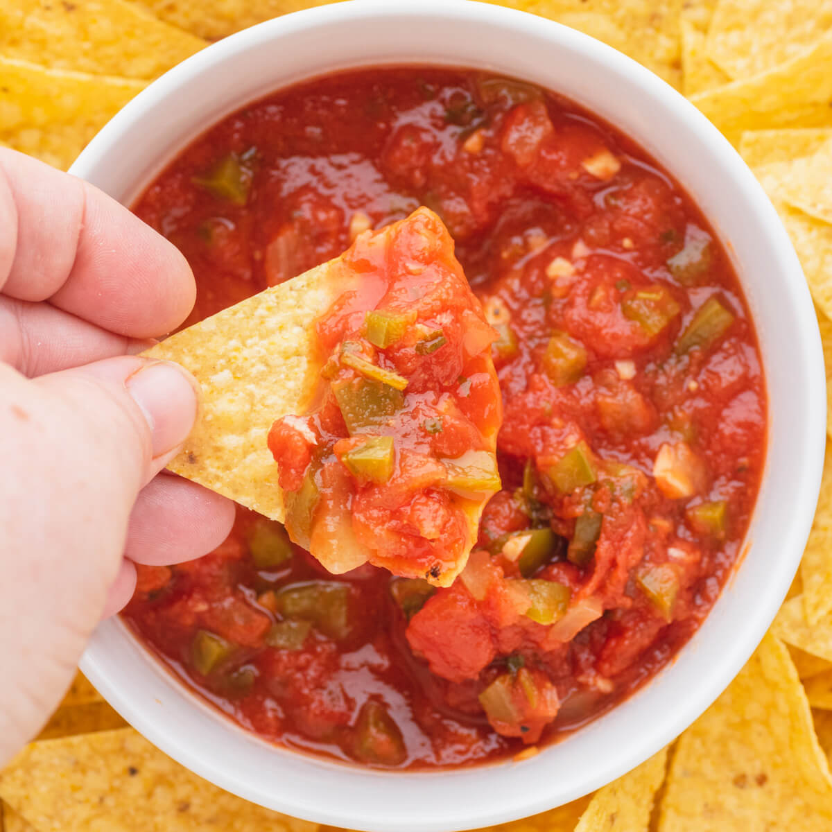 A hand dips a tortilla chip into a bowl of chunky salsa.